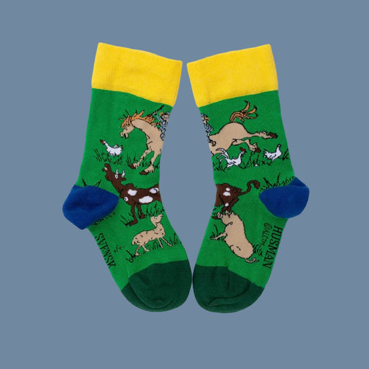 grüne Socken mit dunkelgrünen Spitzen, blauen Fersen und gelben Bündchen mit Tieren vom Katthulthof vor mysblauem Hintergrund