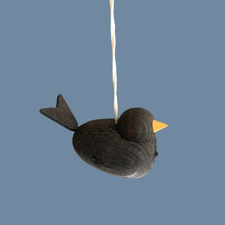 Vogel klein, dunkelgrau aus Holz mit Band vor mysblauem Hintergrund