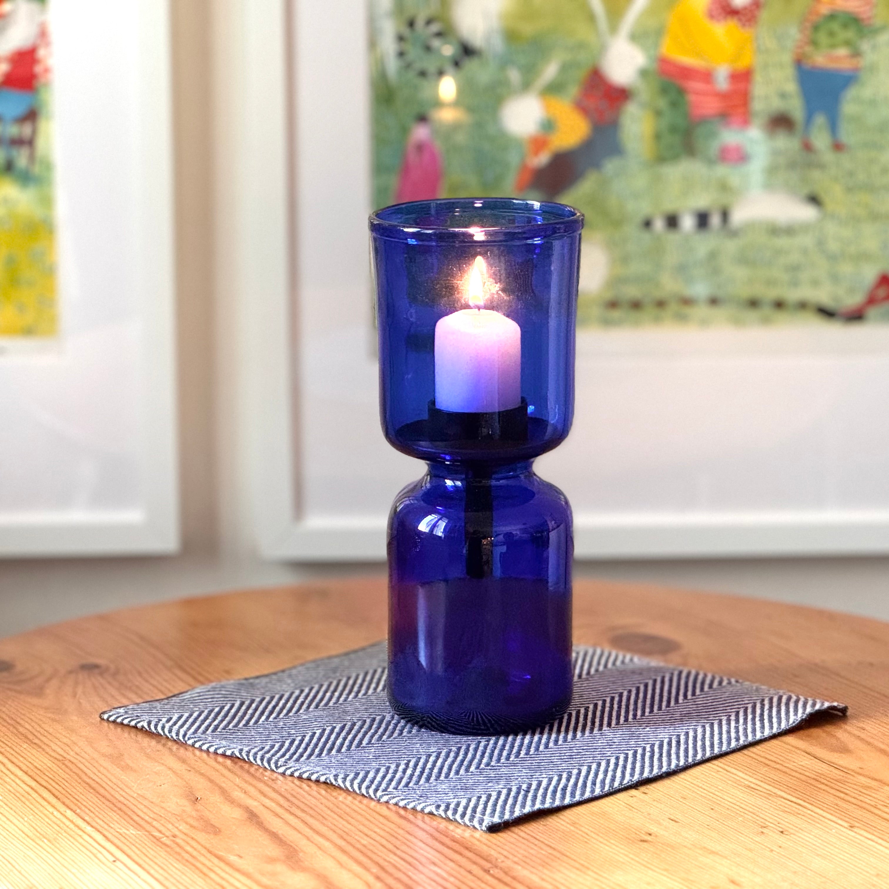 blaues Windlicht aus Glas auf Holztisch mit Bildern im Hintergrund