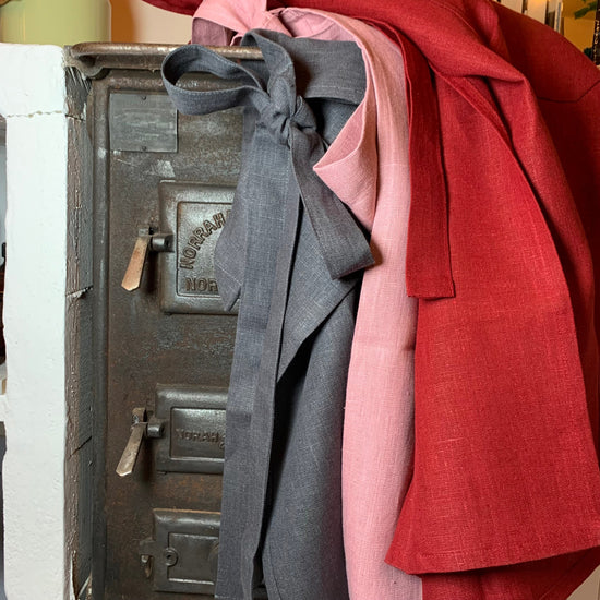 drei Bistroschürzen am Holzherd in je grau, rosa und rot