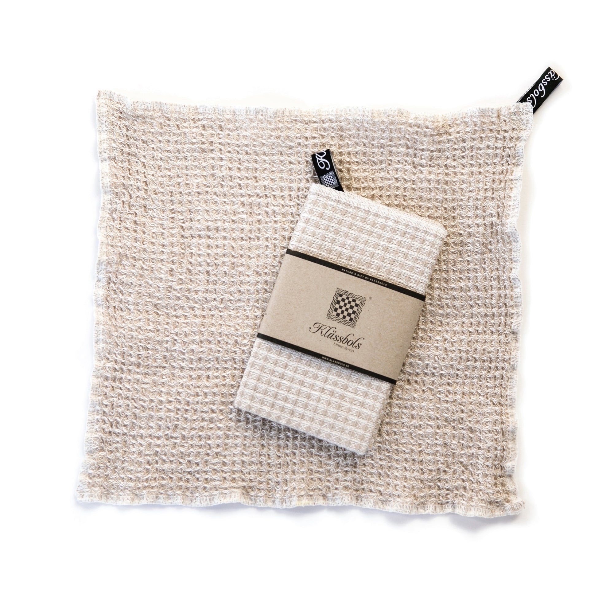 ein gewaschenes Spültuch Bubbel sand Leinen Klässbols linneväveri Mys Shop mit einem neuen Spültuch mit Banderole obenauf liegend