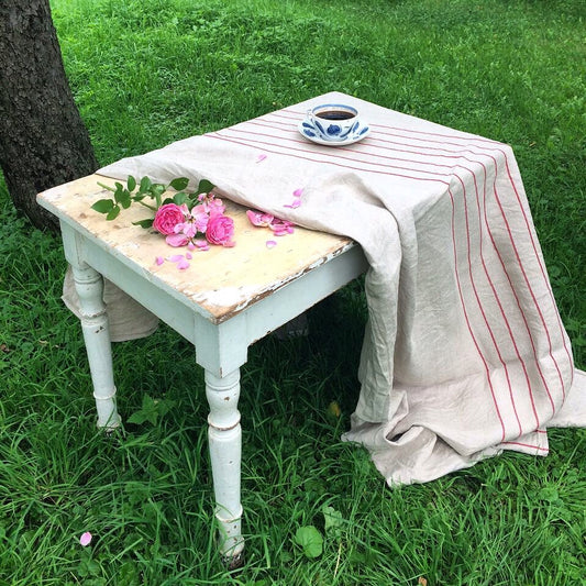Tischtuch "Gärdet" aus Leinen liegt über einer Tischhälte, auf dem Rosen liegen udn eine Kaffeetasse steht