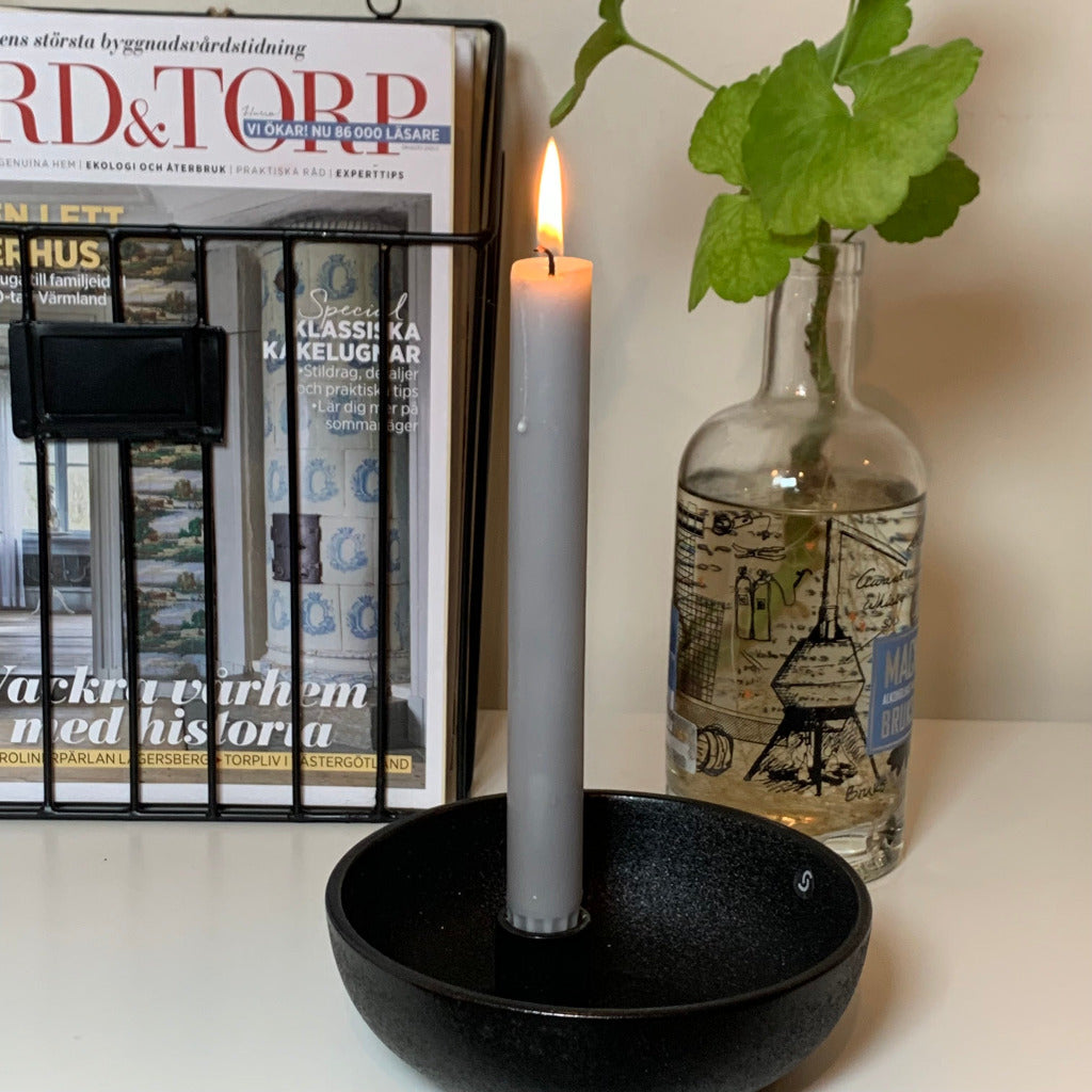 Zeitschriftenhalter mit Zeitschriften davor ein Kerzenhalter aus Keramik und eine Flasche mit Pelargoniensprössling